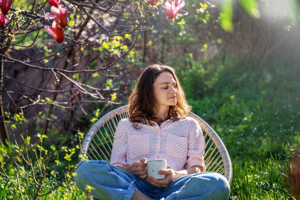 Frau entspannt mit Kaffeetasse im grünen Garten unter einem Magnolienbaum